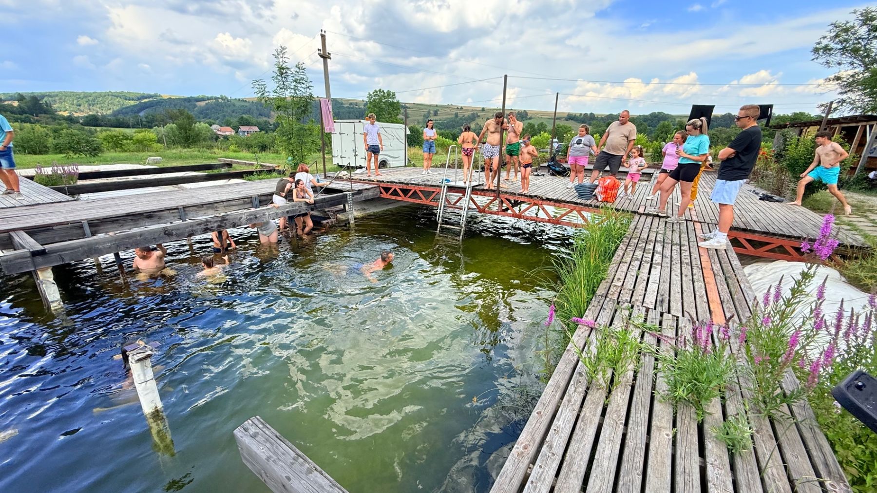 Merülőhely stégjei nyári napon, fürdőző és merülésre készülő közösséggel